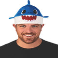 Man wearing Rubie's Baby Shark Hat with Original Song Sound Chip, blue shark design with white belly and red teeth.